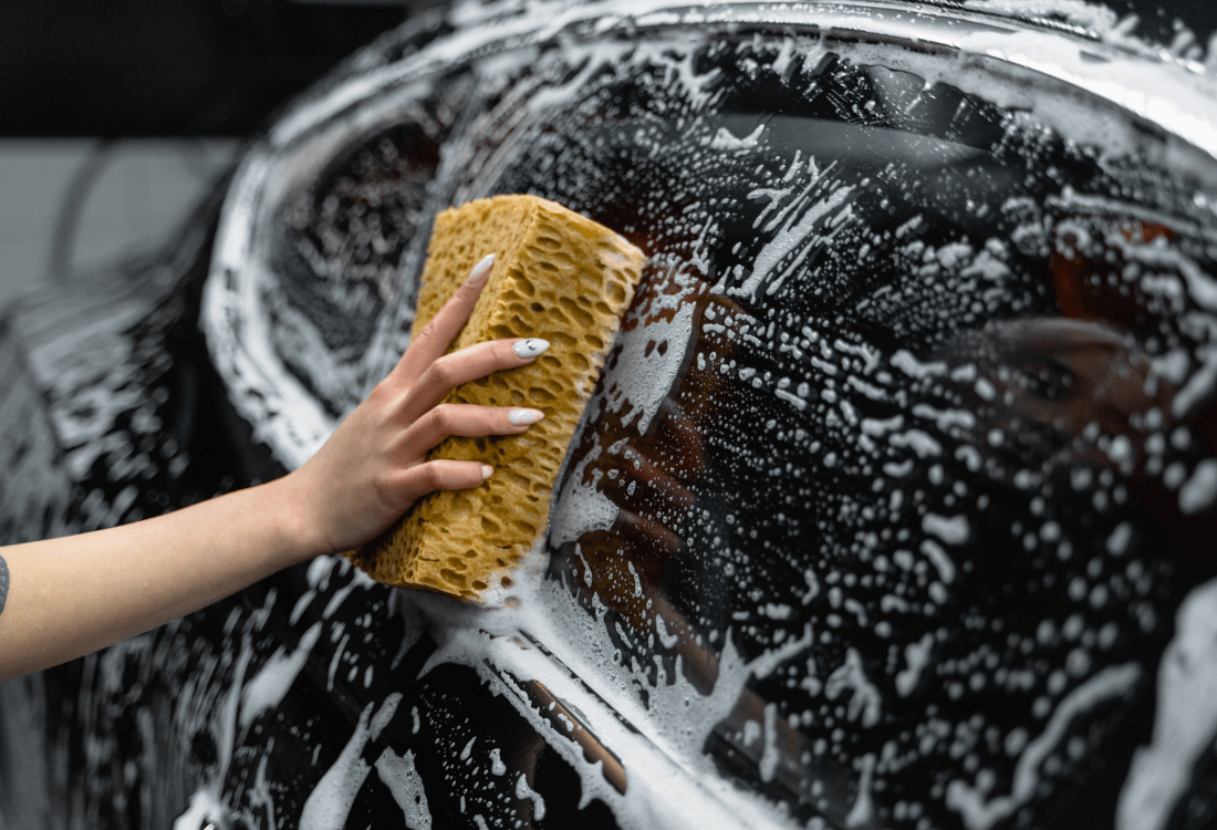 A person using cleaning products and a sponge to clean a car window experiencing the advantages of the car cleaning chemicals market 